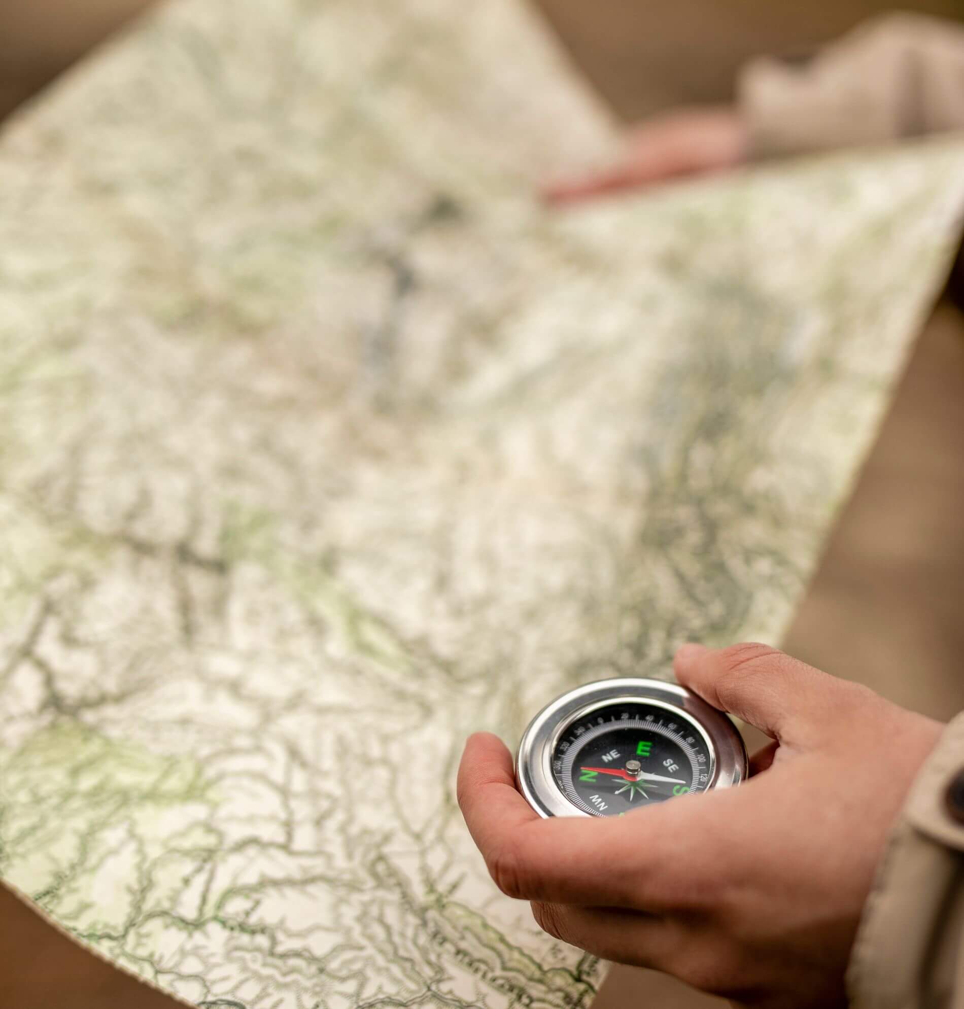 Hands using a compass on a topographic map in the wilderness.
